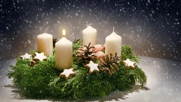 Ein Adventskranz mit vier Kerzen, Tannenzweigen, Zapfen und Sternen. Die erste Kerze brennt. Der Ursprung des Adventskranzes liegt im 19. Jahrhundert.