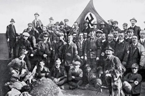 Grupa mężczyzn w mundurach i kapeluszach, z flagą NSDAP w tle. To zdjęcie pokazuje członków partii nazistowskiej, czyli NSDAP.