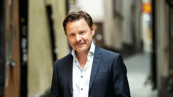 Kasper Sulocki, en man med mustasch, bär en mörkblå rutig kavaj och vit skjorta i en gränd.