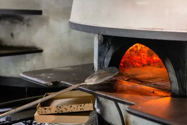 Piec do pizzy z rozżarzonymi węglami. Łopata gotowa do włożenia ciasta, by piec pizzę w 200 stopniach.