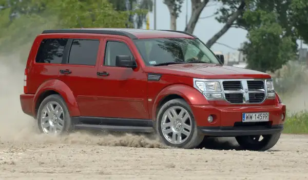 Czerwony Dodge Nitro z impetem wjeżdża na piaszczystą drogę, wzbijając tumany kurzu.