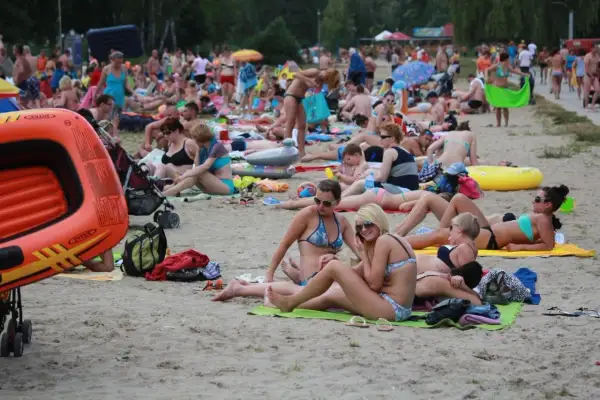 Tłum ludzi odpoczywa na plaży nad jednym z lubelskich jezior. Wszyscy w strojach kąpielowych, opalają się i relaksują.