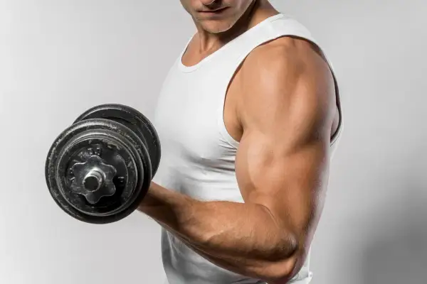 Mężczyzna w białej koszulce podnosi ciężarek, ćwicząc biceps. Zastanawiasz się, ile razy w tygodniu ćwiczyć biceps?