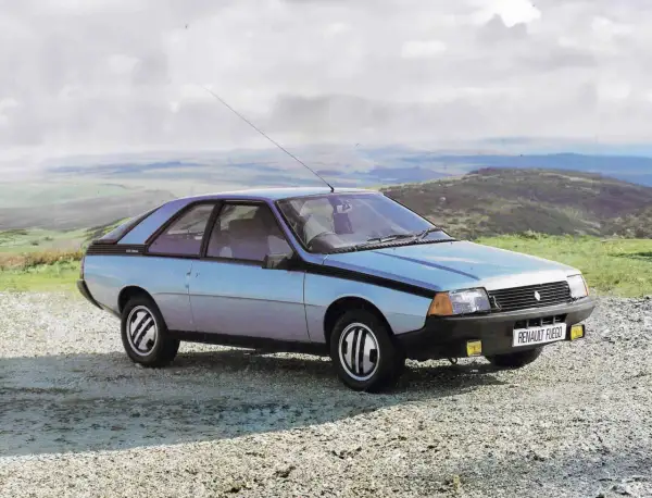 Jasnoniebieski Renault Fuego z lat 80. stoi na szutrowej drodze, z widokiem na pagórkowaty krajobraz i chmurne niebo.
