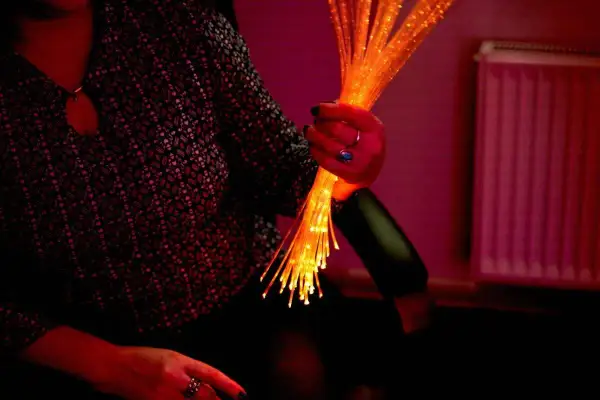 Une main tient un bouquet de fibres optiques lumineuses, évoquant l'univers apaisant du snoezelen.