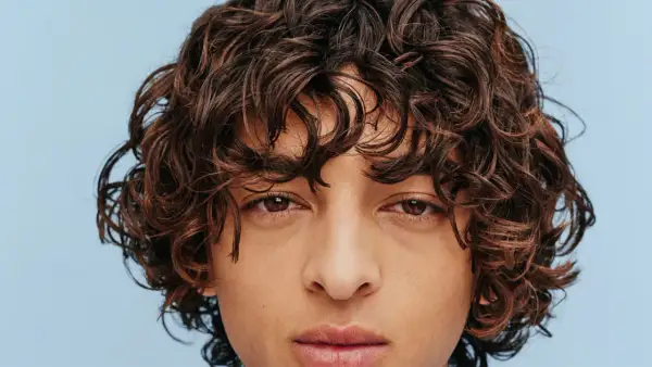 Gros plan sur le visage d'un homme aux cheveux bruns ondulés, type cheveux 2b homme, sur fond bleu clair.