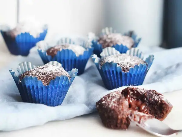 Kladdkakemuffins recept: Mjuka chokladmuffins i blåa pappersformar, pudrade med florsocker. En är uppskuren och visar en härligt kladdig insida.