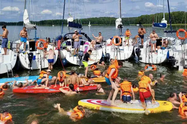 Ludzie w kamizelkach ratunkowych i strojach kąpielowych pływają i bawią się na deskach SUP przy żaglówkach. Wspaniały weekend czerwcowy na wodzie.