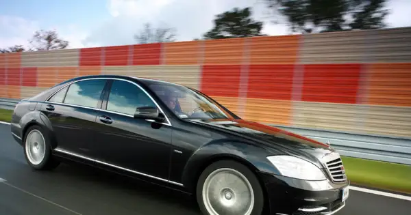 Czarny Mercedes S400d pędzi autostradą obok kolorowego ekranu dźwiękochłonnego.