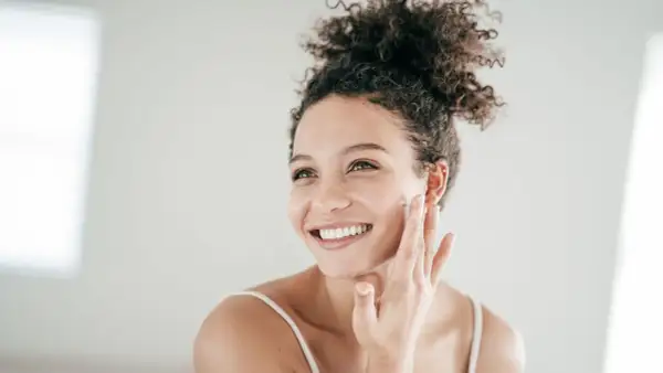 Mujer sonriente aplicándose crema, un paso esencial para el cuidado de piel grasa.
