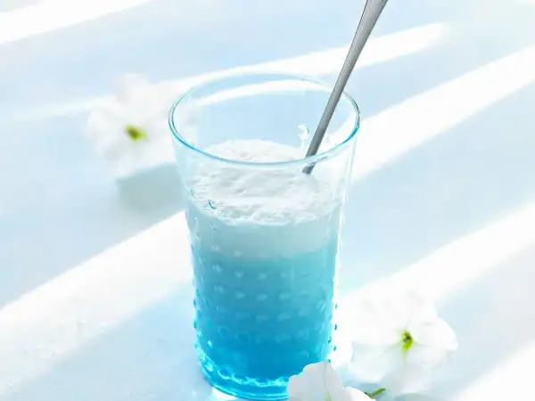 Ein erfrischender Blue Curacao Cocktail in einem strukturierten Glas, garniert mit weißen Blüten.