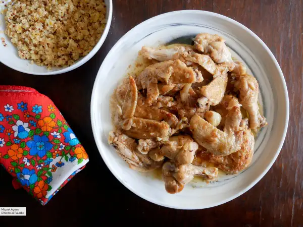 Alitas de pollo al ajillo, doradas y jugosas, servidas en un plato blanco. Acompañadas de quinoa y una servilleta colorida.
