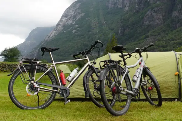 Twee fietsen staan klaar voor een fietsvakantie, met een tent en bergen op de achtergrond.