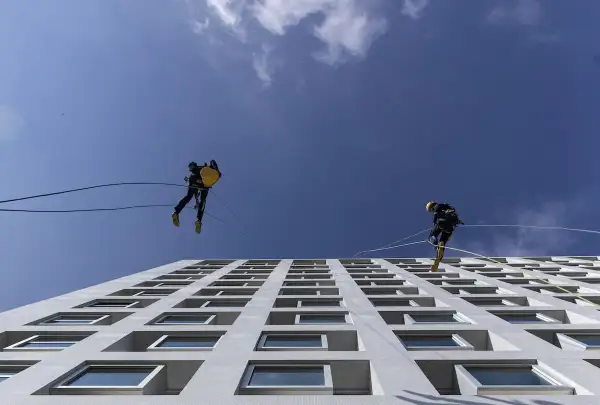Lavoratori in corda assicurati da una linea vita tetto obbligatoria scendono lungo la facciata di un edificio moderno.