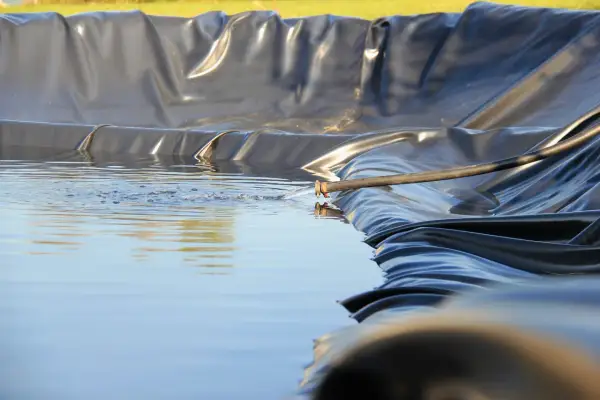 Wasser fließt aus einem Schlauch in einen neu angelegten Folienteich.