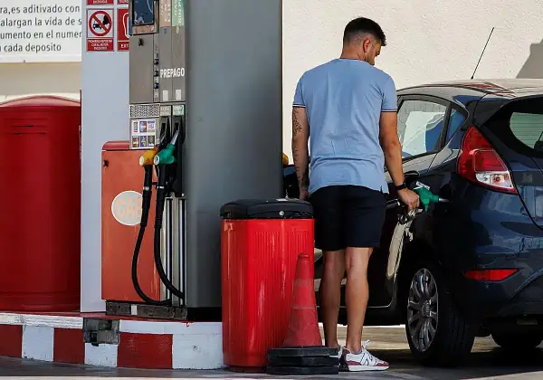 Hombre repostando su coche con gasolina 98. El surtidor muestra opciones de combustible, incluyendo la opción de alta octanaje.
