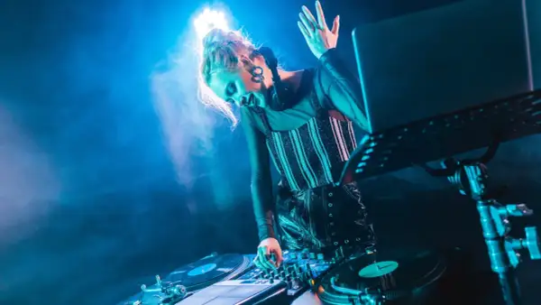 DJka w świetle niebieskich reflektorów tworzy energetyczną muzykę elektroniczną, miksując dźwięki na konsoli.