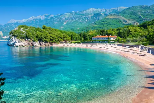 Malownicza zatoka z piaszczystymi plażami w Czarnogórze. Turkusowa woda, zielone wzgórza i biały budynek hotelu tworzą idylliczny krajobraz.