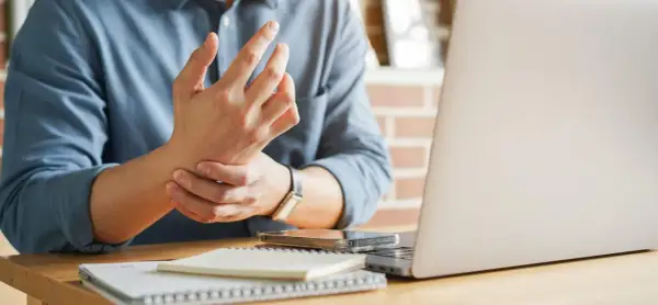 Uomo con male ai polsi mentre lavora al computer. Dolore al polso da uso prolungato del mouse e tastiera.