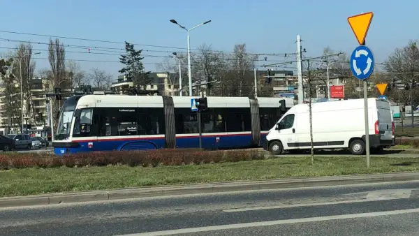 Tramwaj na rondzie, obok biała furgonetka. Czy tramwaj ma pierwszeństwo na rondzie? Znak informuje o ruchu okrężnym.