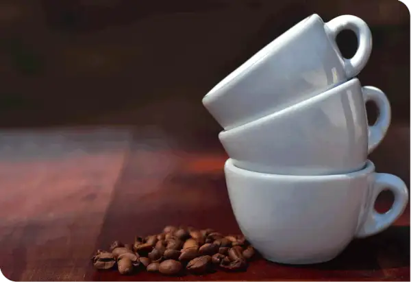 Tre tazzine bianche impilate e chicchi di caffè. Una tazzina di caffè contiene circa 60 ml.