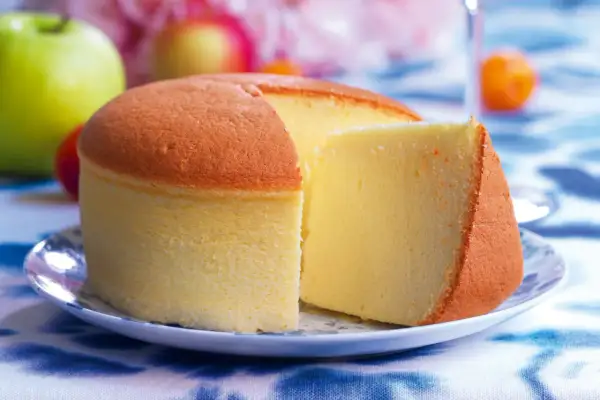 Una soffice torta di cotone, dorata e leggera, servita su un piatto con mele verdi e rosse sullo sfondo.