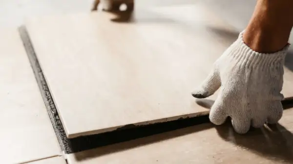 A gloved hand places a tile. Walking on tile too soon can cause shifting and unevenness.