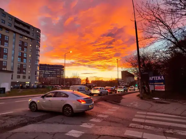 Spektakularny zachód słońca Kraków maluje niebo na pomarańczowo i różowo nad ulicą z samochodami i blokami.
