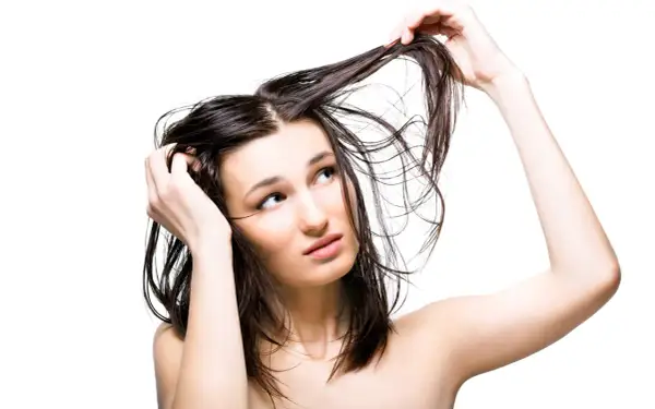 Jeune femme aux cheveux gras, se touchant la tête, l'air interrogateur. Pourquoi ces cheveux gras ?