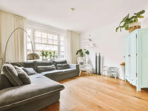 Gemütliches kleines Wohnzimmer einrichten mit großem Ecksofa, Bogenlampe, Pflanzen und mintgrünem Schrank.