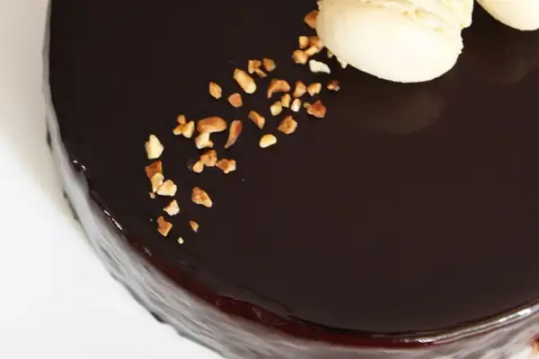 Gâteau au glacage chocolat brillant, parsemé de noisettes concassées et décoré de macarons.