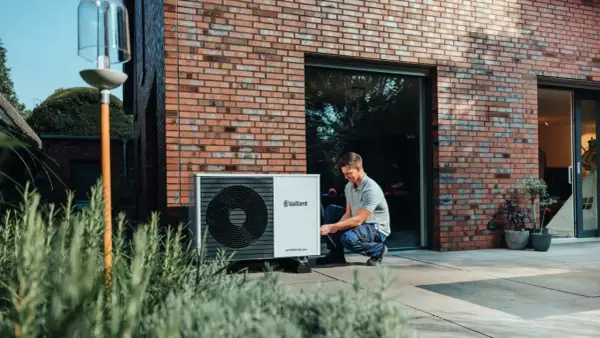Installazione di una pompa di calore esterna: un uomo controlla l'unità posizionata vicino alla casa.