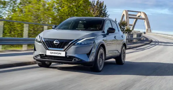 Szary Nissan Qashqai 2024 pędzi po moście z łukowatym wiaduktem w tle.