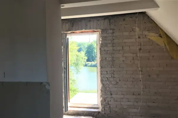 Trwa wymiana okien w domu z widokiem na jezioro. Widać surowe ściany i piankę montażową.