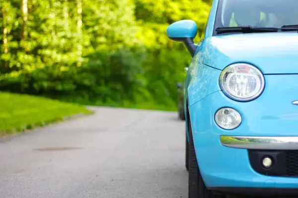 Niemiecki cepik, błękitny Fiat 500, parkuje na krętej drodze wśród zieleni.