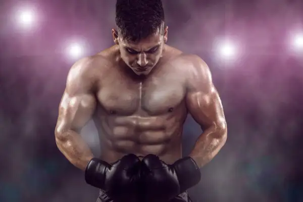 A muscular boxer with a defined boxer physique, wearing black gloves, looks down intensely under stadium lights.