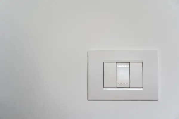 Włącznik Simon 10 czy 54? Biały, nowoczesny panel z trzema przełącznikami na jasnej ścianie.