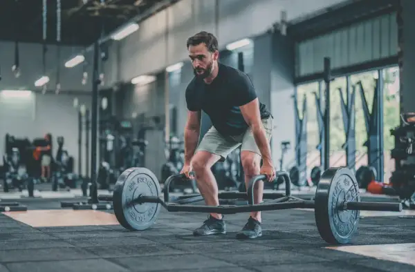 Un homme concentré effectue un dead lift avec une barre hexagonale dans une salle de sport.