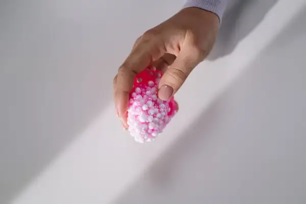 Dłoń trzyma różowy slime z kulkami, który wygląda jak mała, puszysta chmurka.
