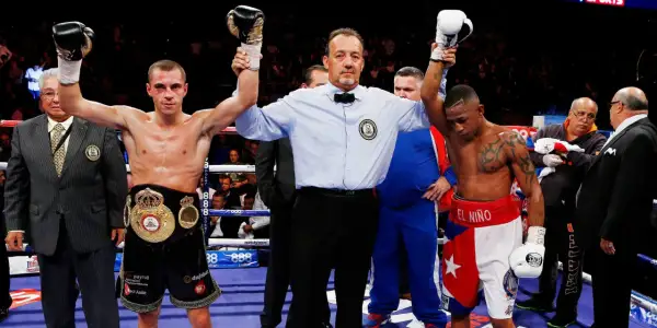 Referee raises the winner's hand after a boxing match. The boxer on the left, wearing a championship belt, achieved a win by decision.