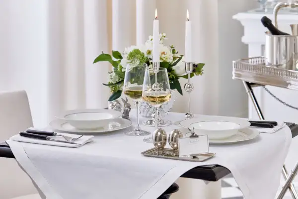 Vacker dukning med vita tallrikar, vinglas och ljus. Frågan "hur stor duk ska man ha" besvaras här med en duk som täcker bordet elegant.