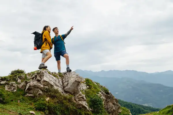 Zwei Wanderer auf einem Felsvorsprung genießen die Aussicht während ihrer Alpen Tour.