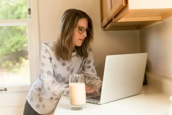 Frau mit Brille am Laptop, studieren mit 40 berufschancen. Ein Glas Milch steht daneben.