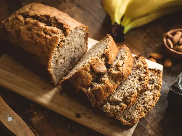 Saftiges Bananenbrot, perfekt für ein Bananenbrot Rezept ohne Zucker. Daneben liegen Mandeln und reife Bananen.