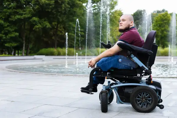 Mężczyzna na wózku inwalidzkim patrzy w dal, siedząc przy fontannie.