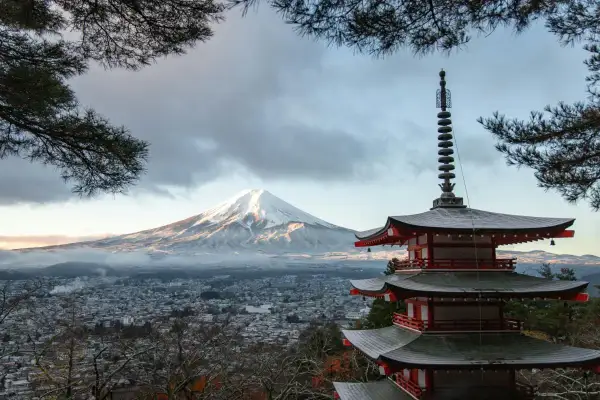 Japanische Regenzeit: Ein schneebedeckter Fuji-san erhebt sich über einer Stadt, daneben eine rote Pagode.