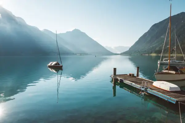 Segelboote am Achensee, ein wahrer Geheimtipp. Berge spiegeln sich im klaren Wasser, ein Steg lädt zum Verweilen ein.