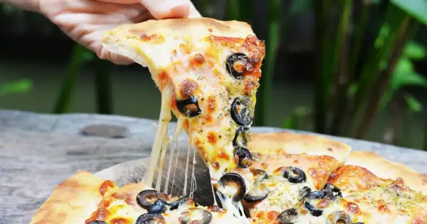 Ciągnący się ser z kawałka pizzy capriciosa z oliwkami, podnoszony ręką.