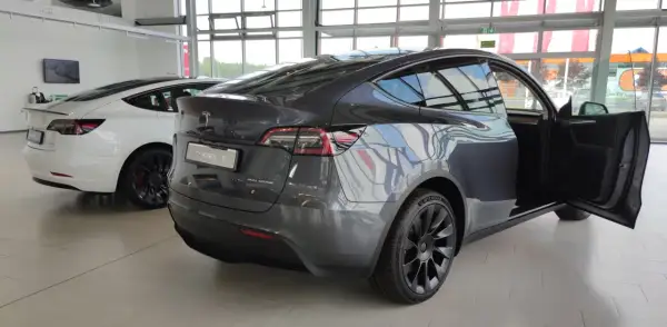 Szary Tesla Model Y z otwartymi drzwiami, obok biały Model 3. Wymiary tego SUV-a są idealne do miasta i na dalsze trasy.