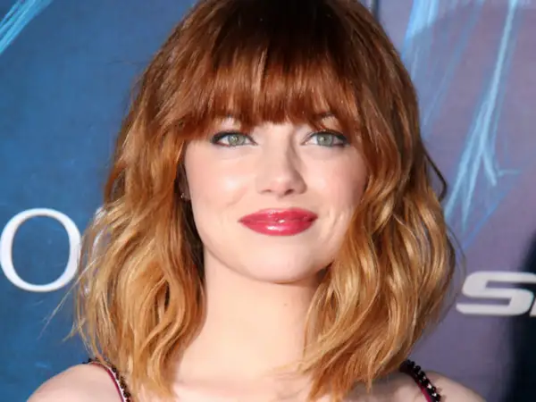 Emma Stone luce un vibrante pelo naranja en cascada, un estilo que realza su belleza natural.